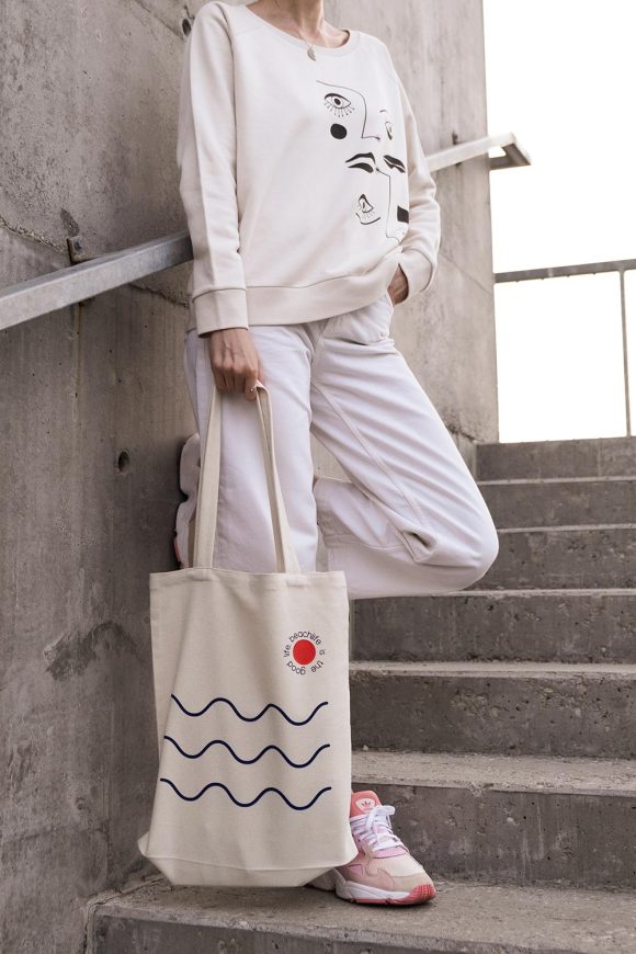 Woman holding a cotton tote bag with waves and sun print from Mauverien.