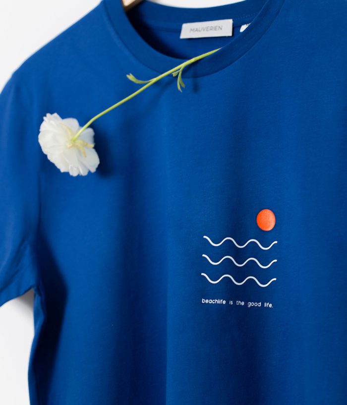 Detaliu print tricou albastru cu 3 linii albe ondulate, 1 cerc mic portocaliu si mesaj beachlife is the good life.