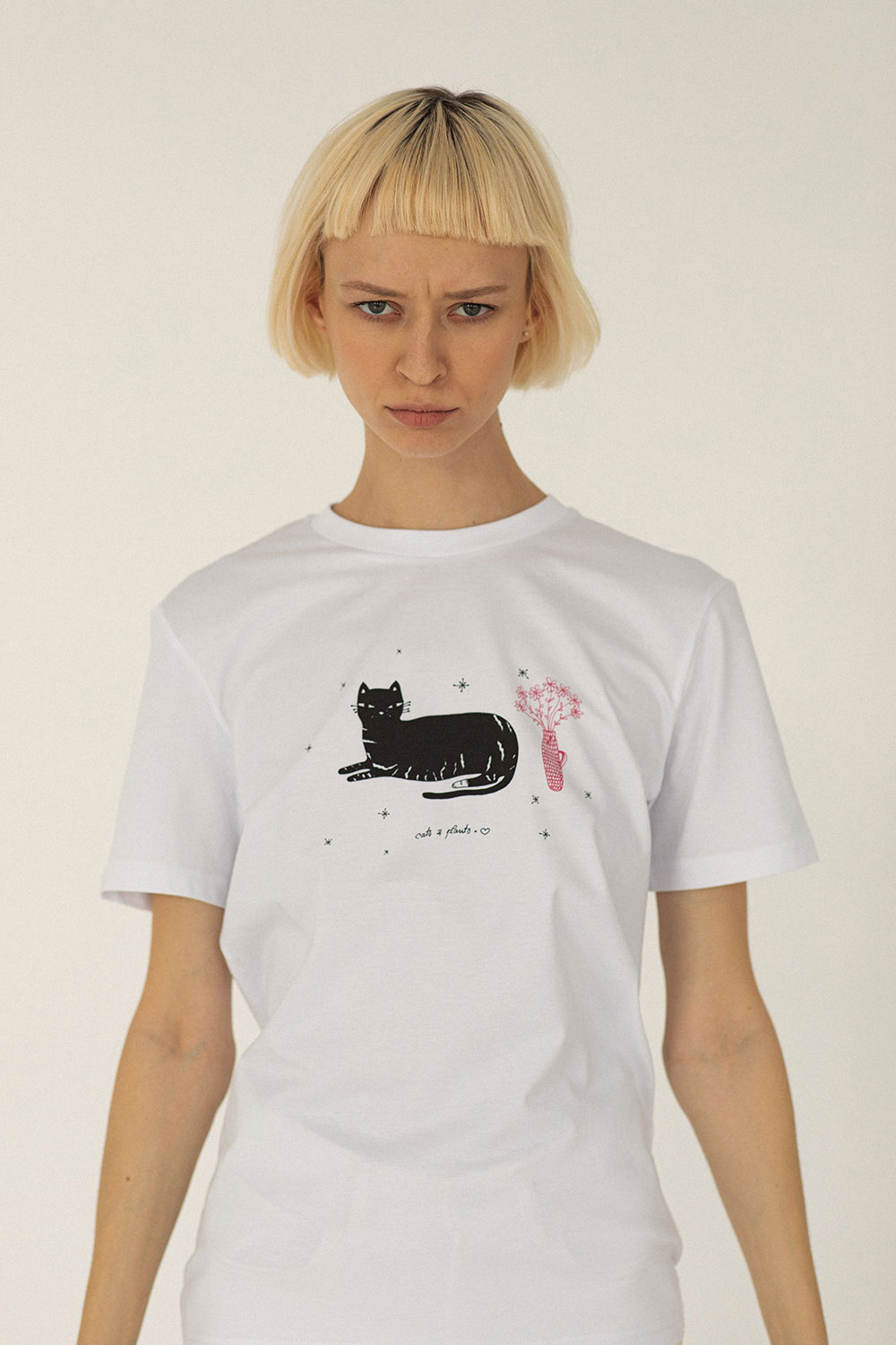 Woman wearing white cotton t-shirt with cat and plant in vase by Romanian brand.
