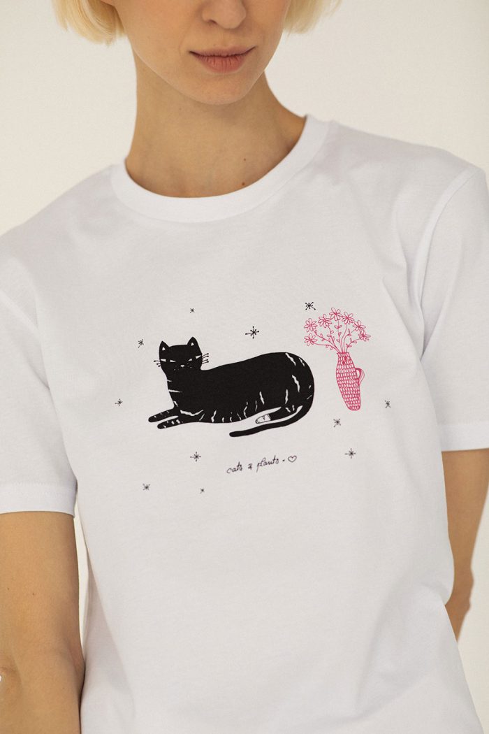 Close-up of white cotton t-shirt printed with black cat and pink flower and vase.