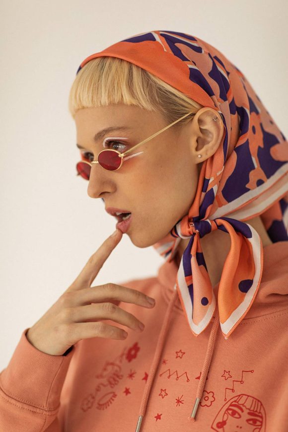 Woman with pink sunglasses & orange hoodie wearing the orange floral scarf from Mauverien.
