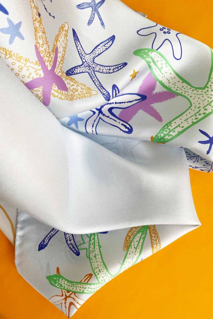 Closeup detail of light blue ocean silk twill scarf with multicoloured starfish pattern.
