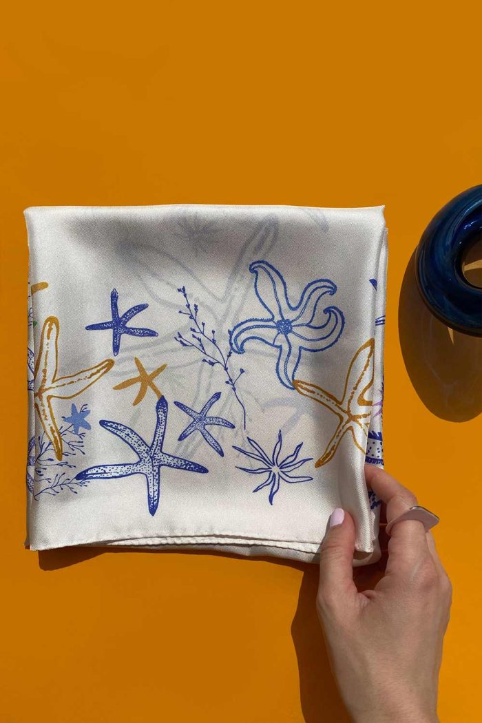 Folded beige silk scarf with starfish pattern created by Romanian designer Mauverien.