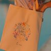 Woman opening the la mer multicoloured cotton tote bag with sea stars and shells by Mauverien.
