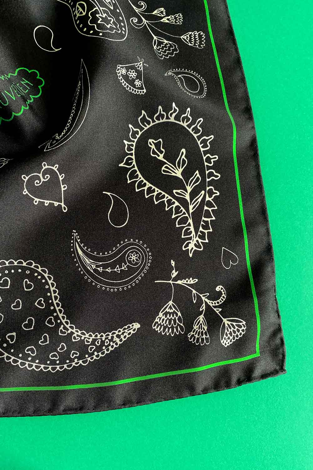 Hand finished detail of black scarf with white and green paisley motif.