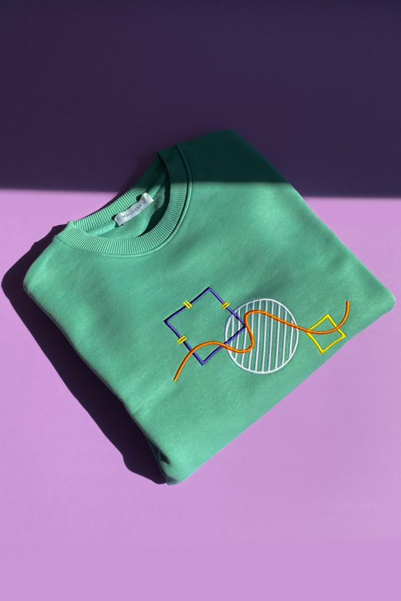 Folded green cotton sweatshirt with abstract shapes embroidered.