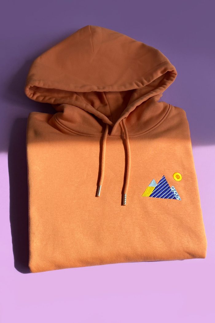 Orange hoodie with mountains embroidery folded.
